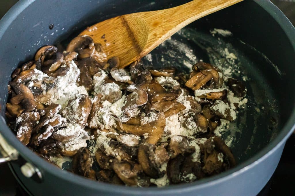 flour sprinkled on mushrooms in a skillet.