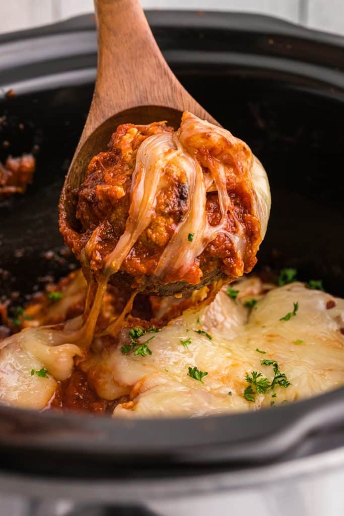 wooden spoon lifting a meatball from a slow cooker.