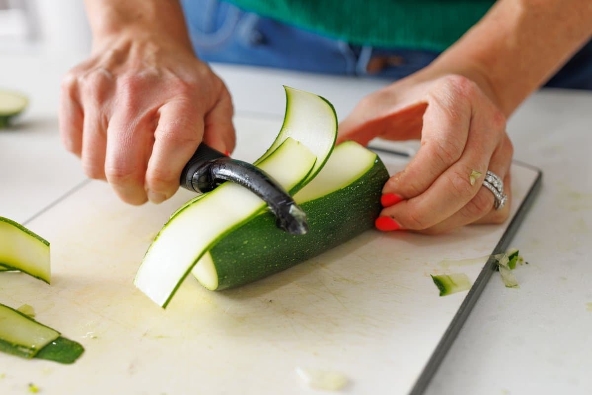 Using a vegetable peeler to slice zucchini into long strips.
