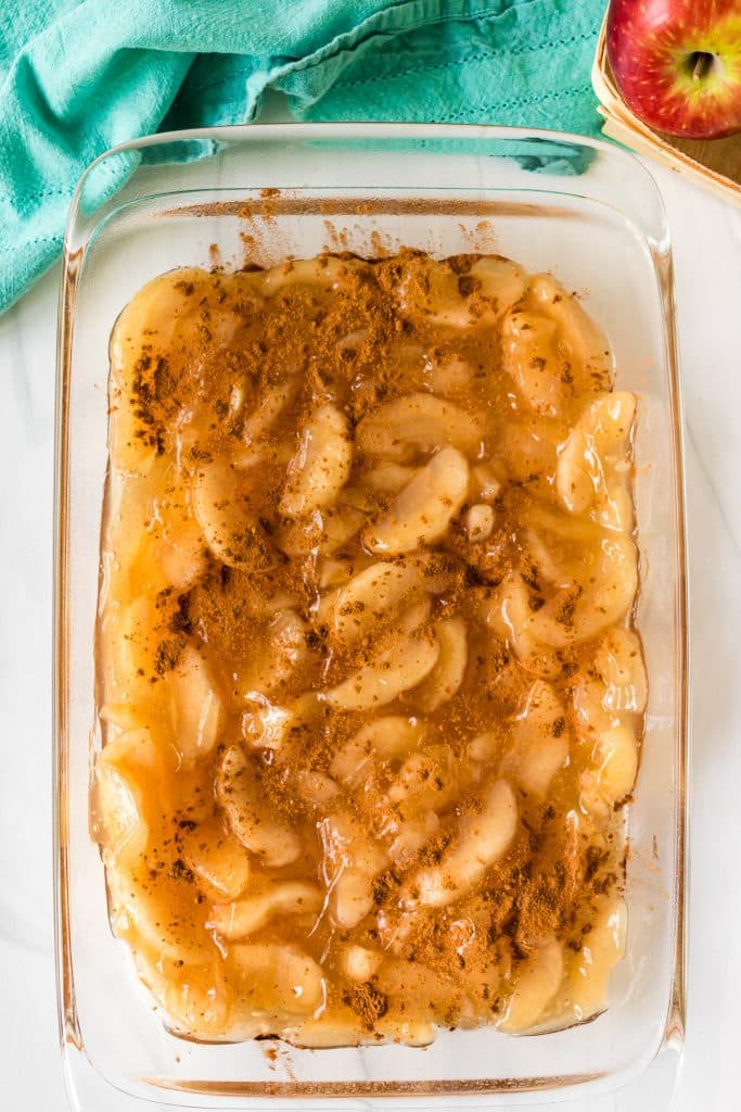 overhead shot of apple pie filling sprinkled with cinnamon in a baking dish.