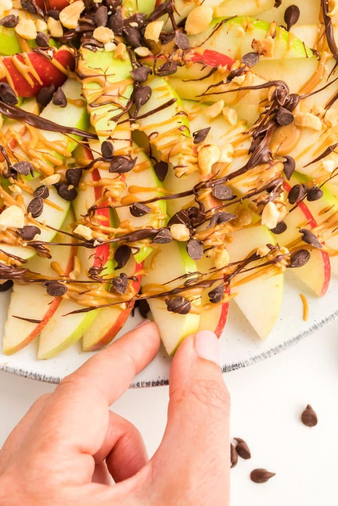 hand lifting a slice peanut butter and chocolate covered apple.