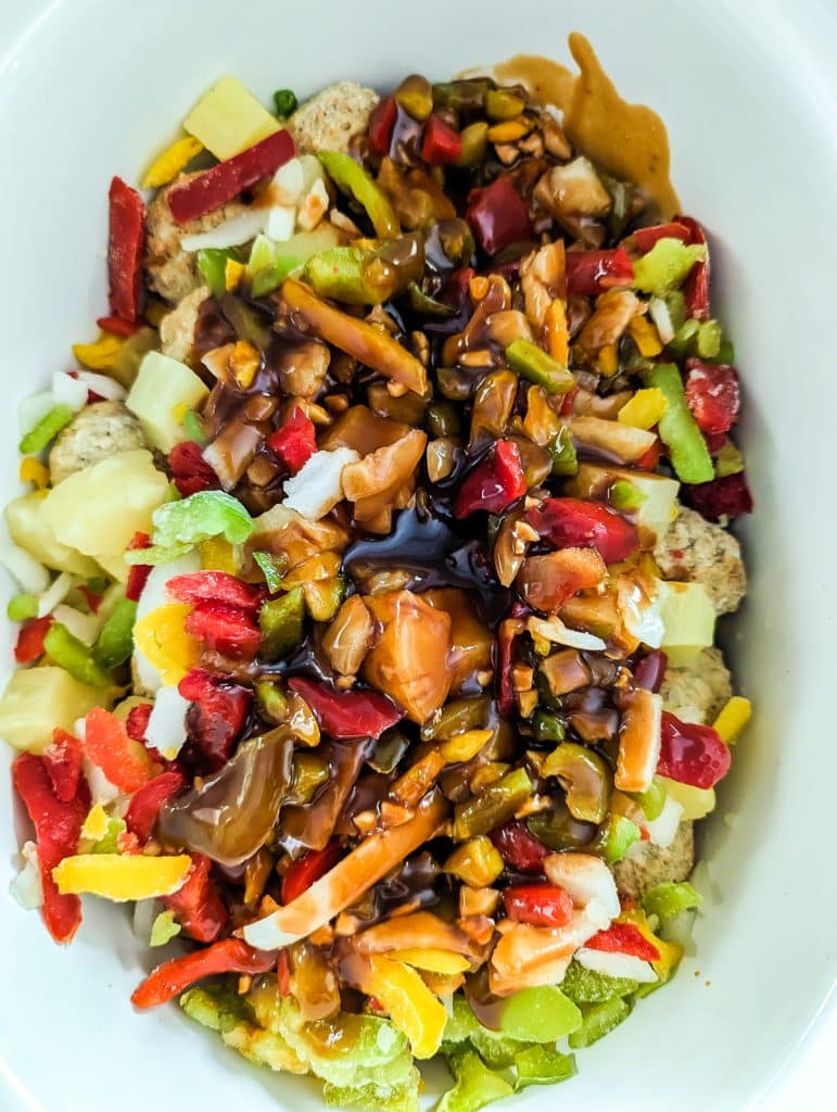 overhead shot of sauce poured onto peppers and onions in a white crockpot.