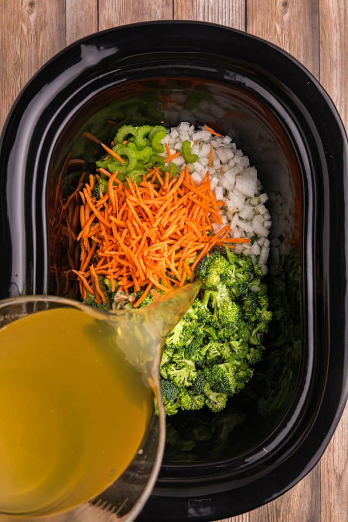 broth pouring into a crockpot of vegetables.