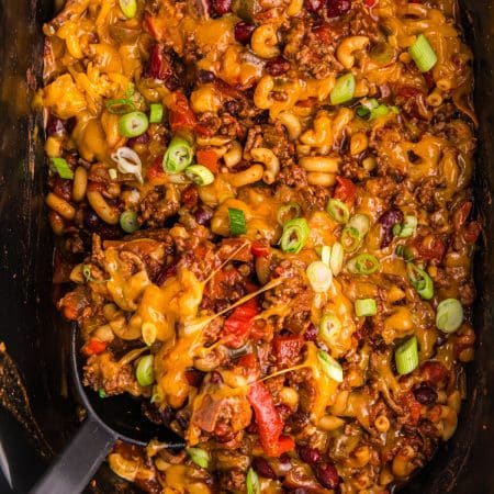 overhead shot of a spoon scooping chili mac from a slow cooker.