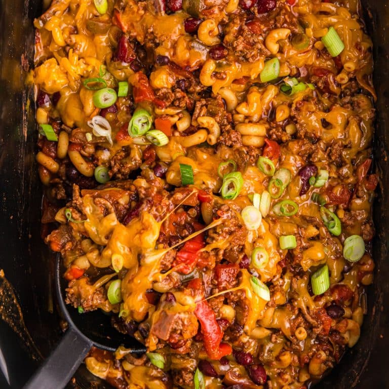 overhead shot of a spoon scooping chili mac from a slow cooker.