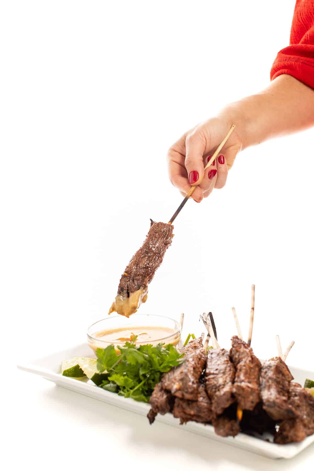 Dipping beef satay skewers with peanut dipping sauce.
