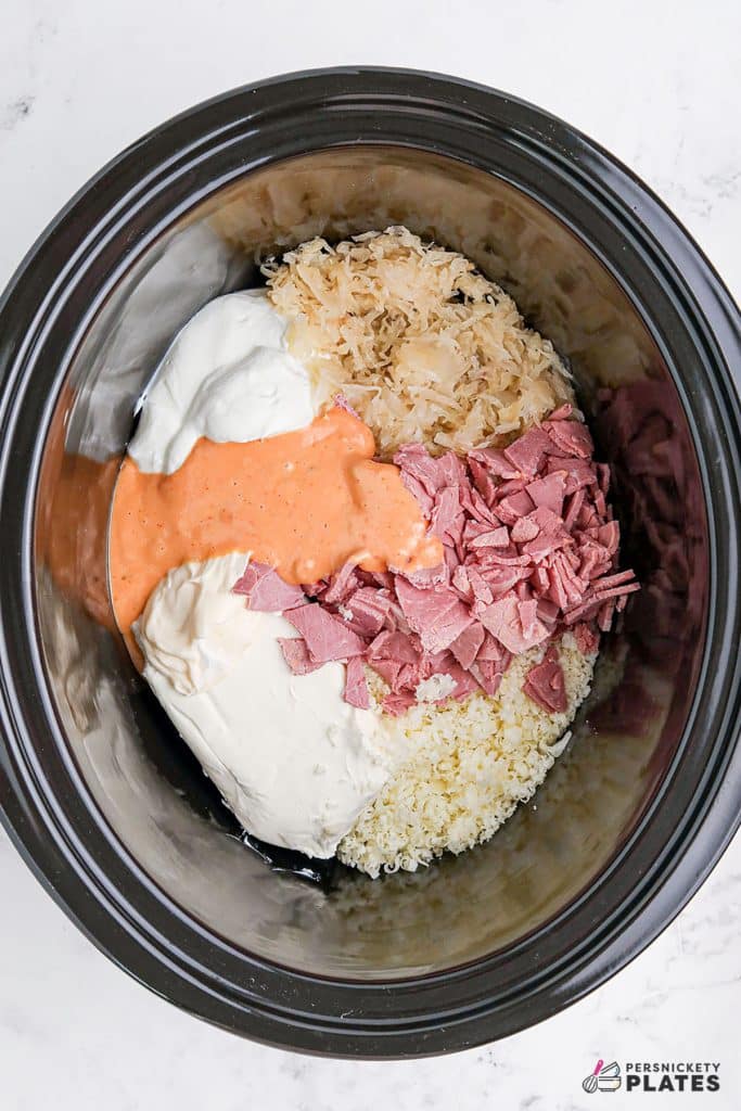 overhead shot of ingredients in a black crockpot making reuben dip.