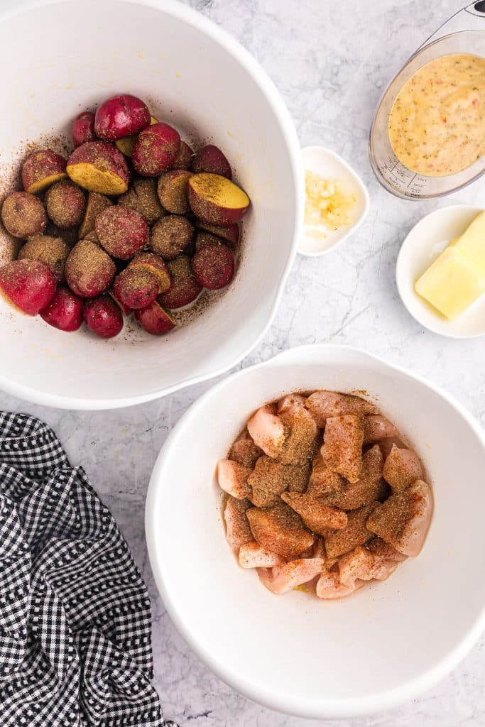 overhead shot of bowls of seasoned raw chicken and seasoned potatoes.