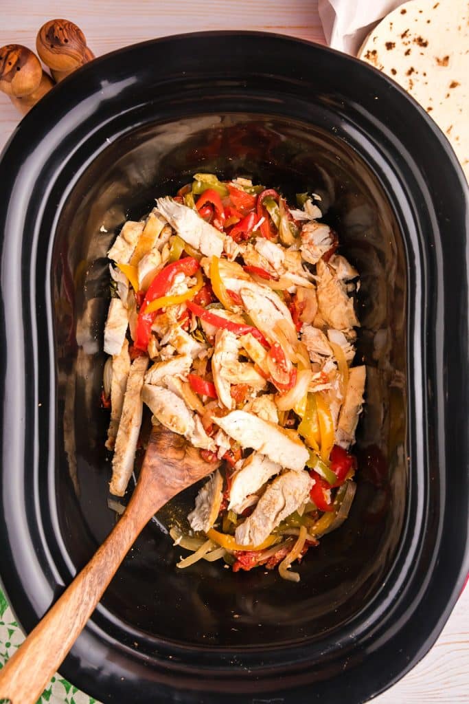wooden spoon in a slow cooker of chicken fajitas.