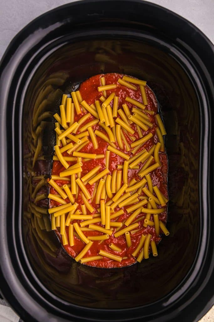overhead shot of uncooked ziti in marinara in a black slow cooker.