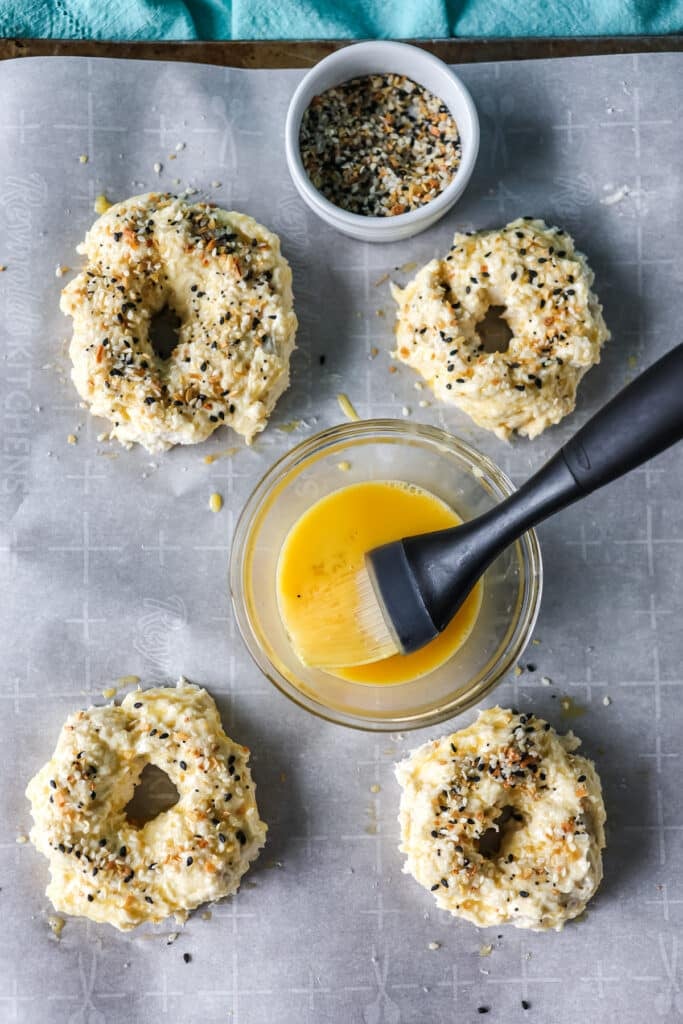 overhead shot of egg wash going onto bagels.