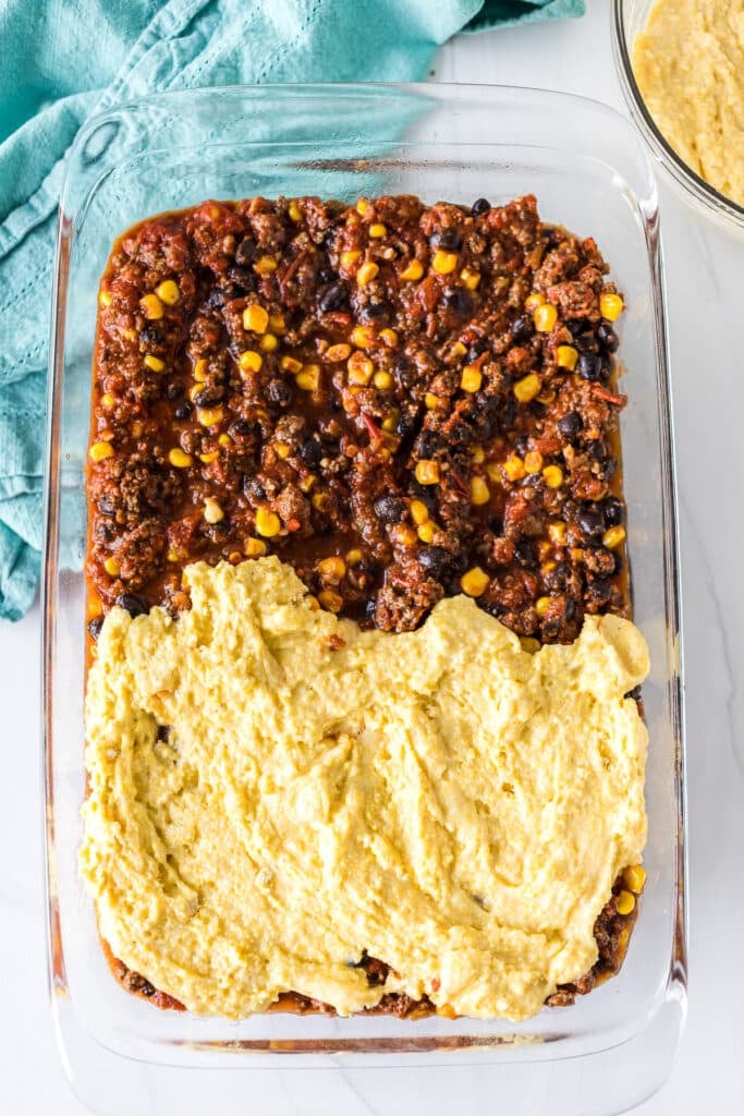 overhead shot of cornbread mix being spread onto a baking dish of chili.