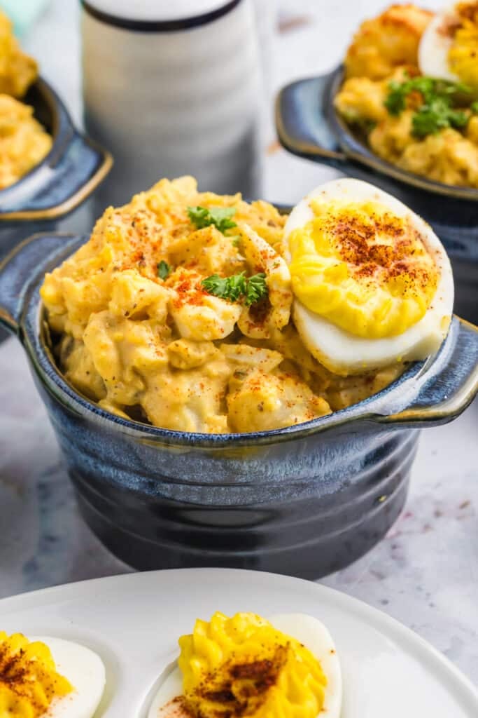 blue bowl of deviled egg potato salad topped with a deviled egg.