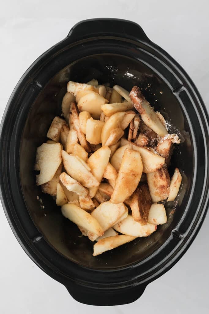 overhead shot of sliced apples and seasonings in a crockpot.