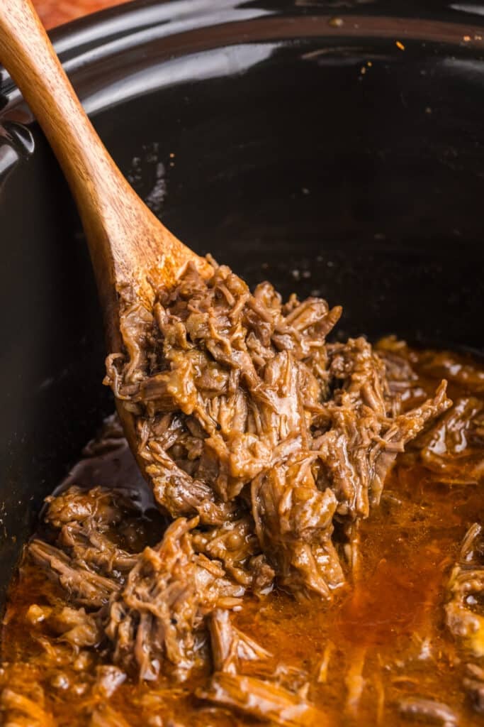 wooden spoon scooping shredded beef from a crockpot.