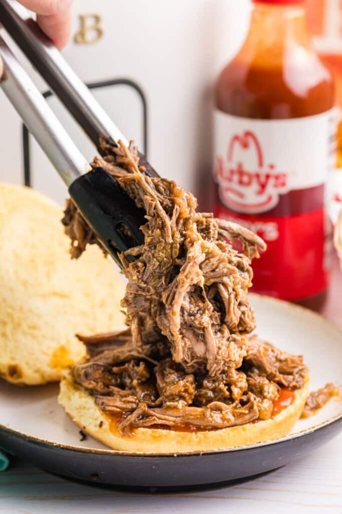 tongs piling shredded beef onto a bun.