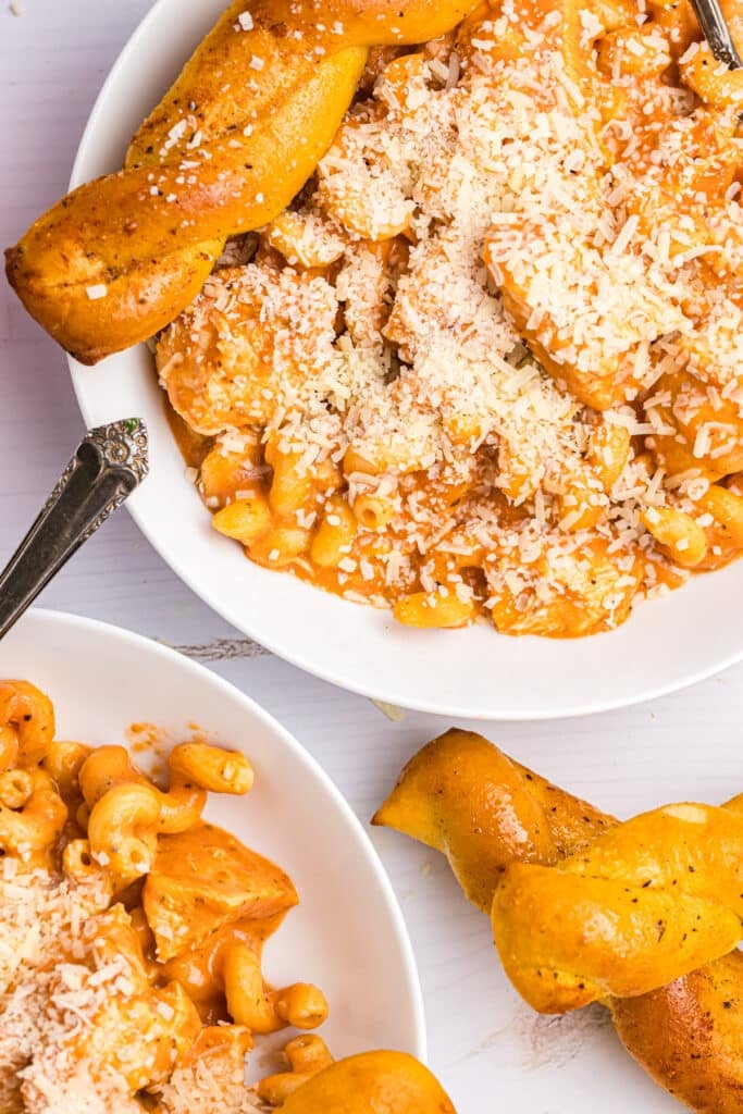 two plates of creamy chicken pasta with breadsticks.