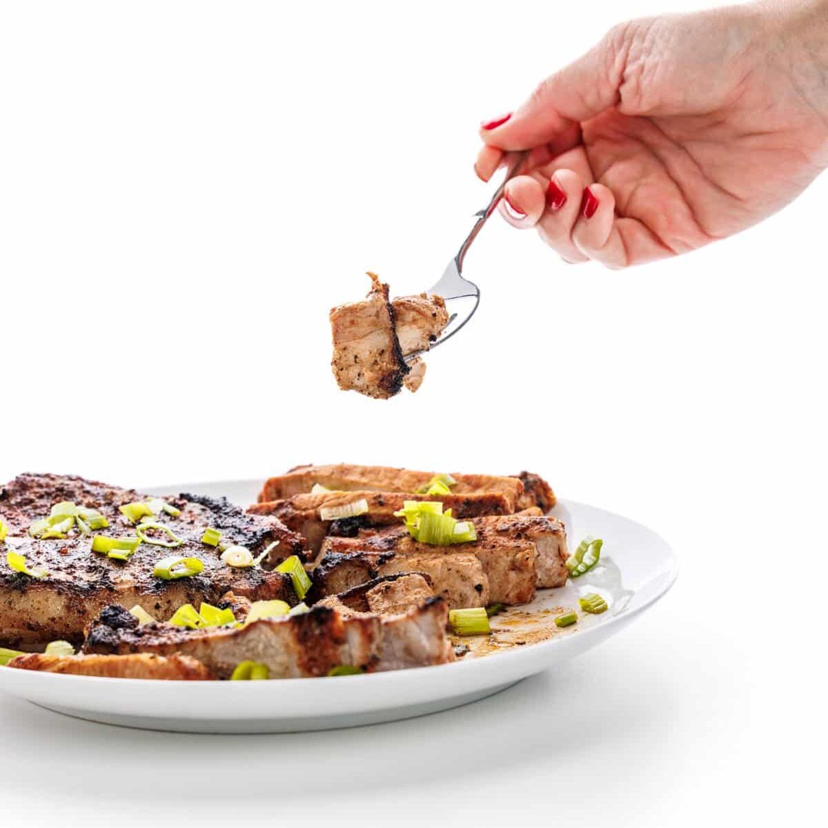 a hand holding a fork over a plate of meat