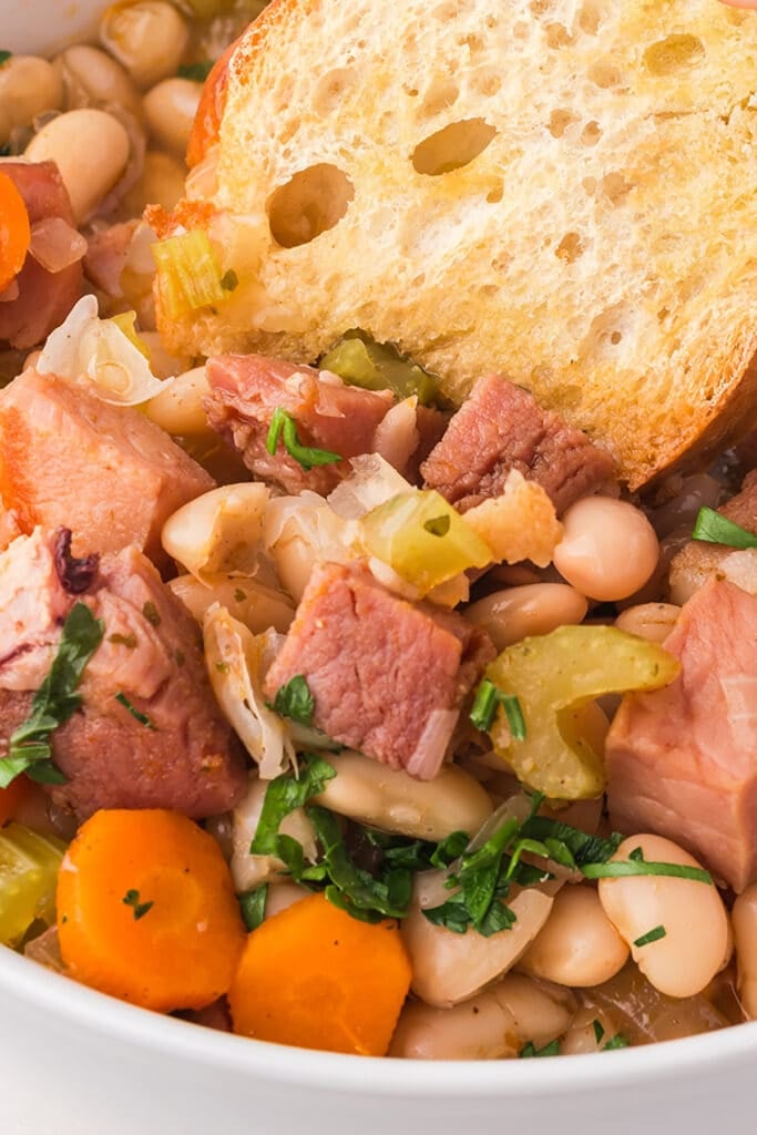 closeup of ham & bean soup with a piece of crusty bread in it.