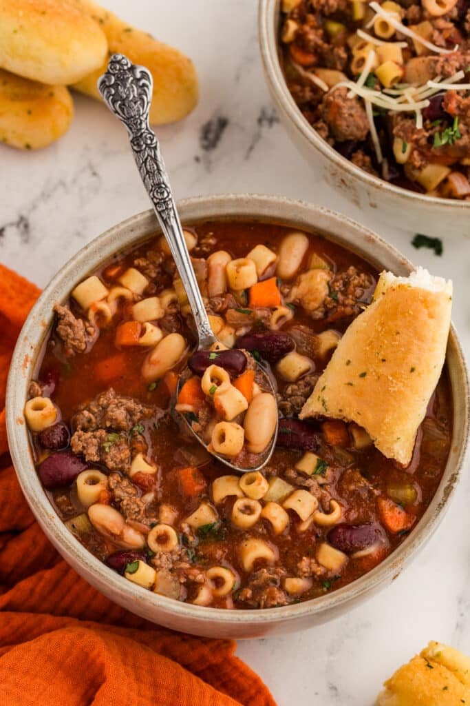 bowl of pasta fagioli soup with a spoon and breadstick in it.