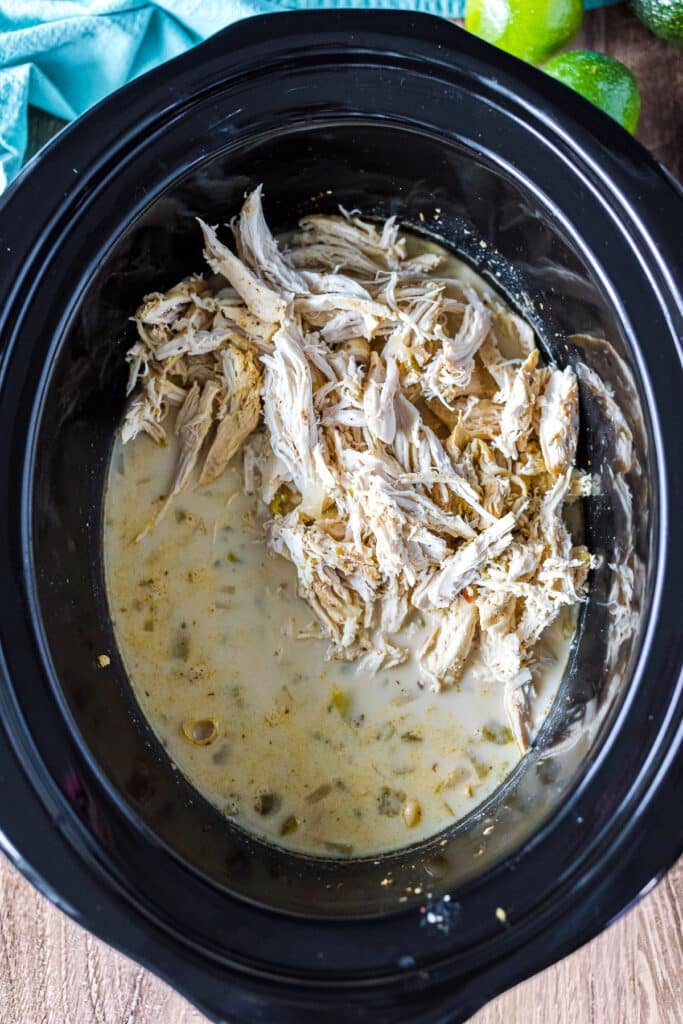 shredded chicken going into a crockpot of chili.
