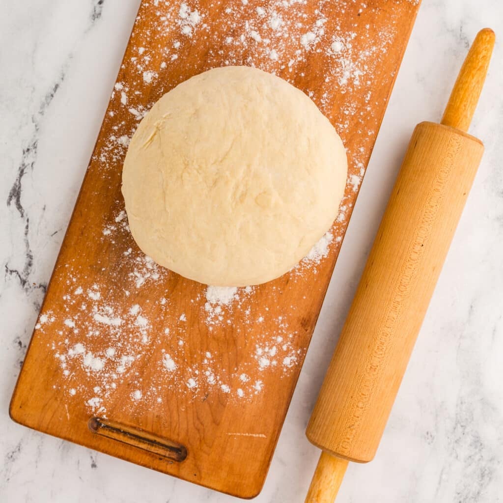 ball of dough on a floured board next to a rolling pin.