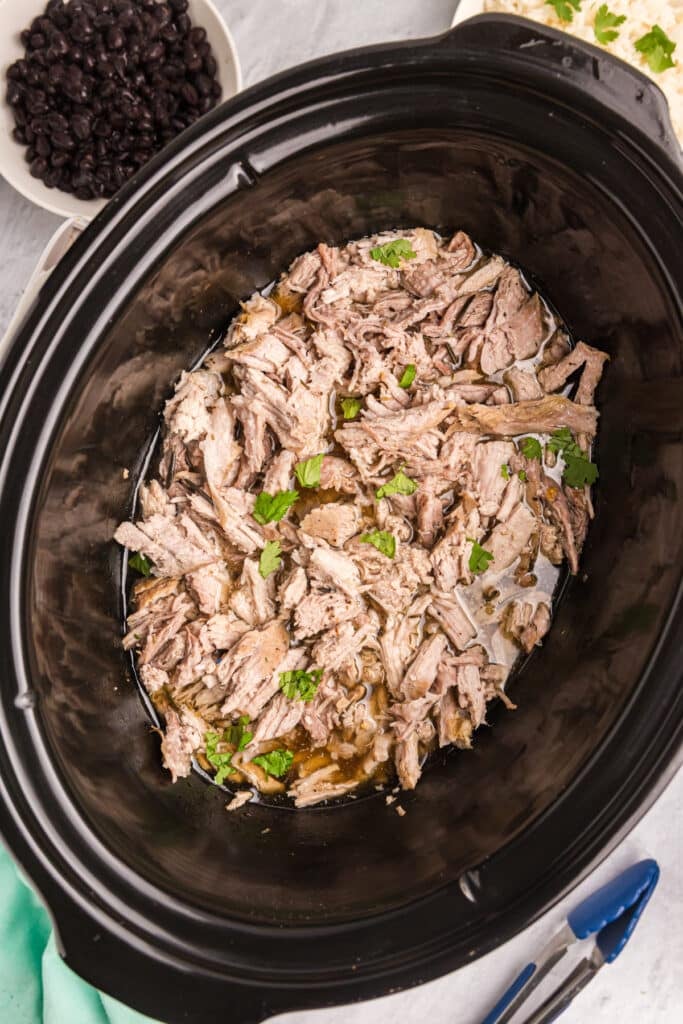 shredded carnitas in a black crockpot.