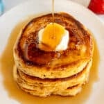 syrup drizzling over a stack of buttered pancakes.
