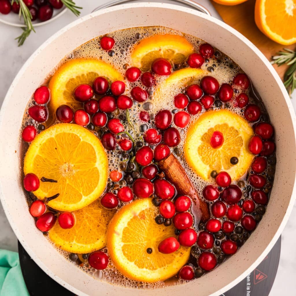 A pot with orange slices, cranberries, rosemary, and cinnamon sticks in liquid.
