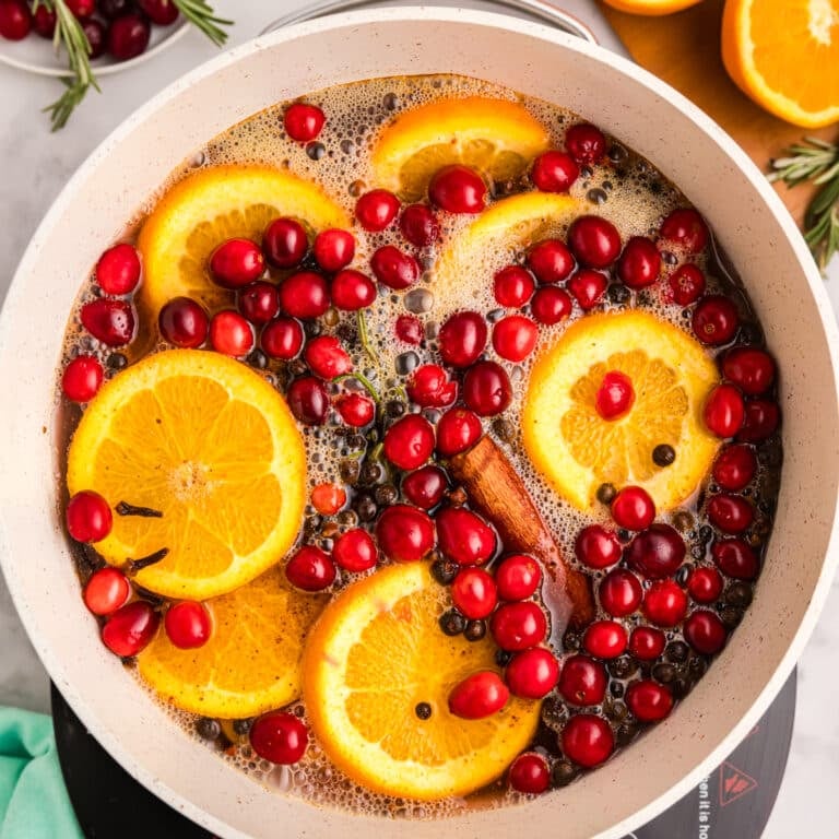 A pot with orange slices, cranberries, rosemary, and cinnamon sticks in liquid.