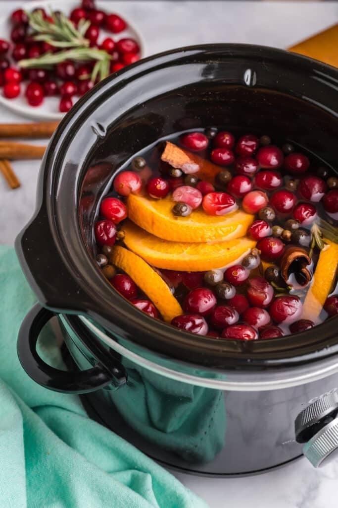 overhead shot of a black slow cooker filled with sliced oranges, cranberries, cinnamon sticks, and spices.