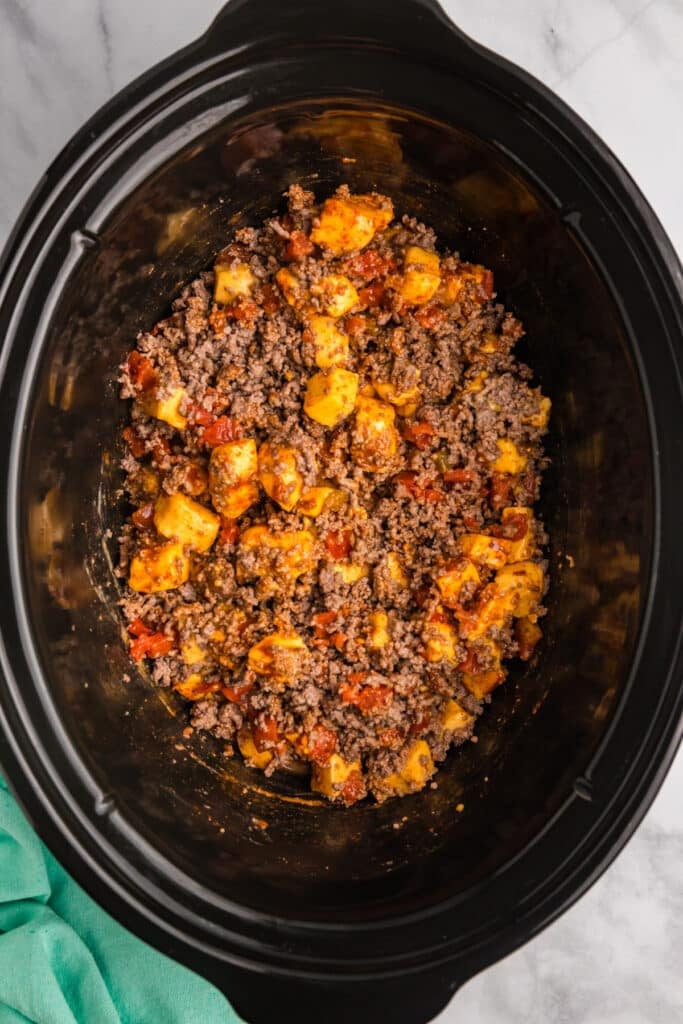 overhead shot of velveeta cubes, ground beef, and rotel in a crockpot.