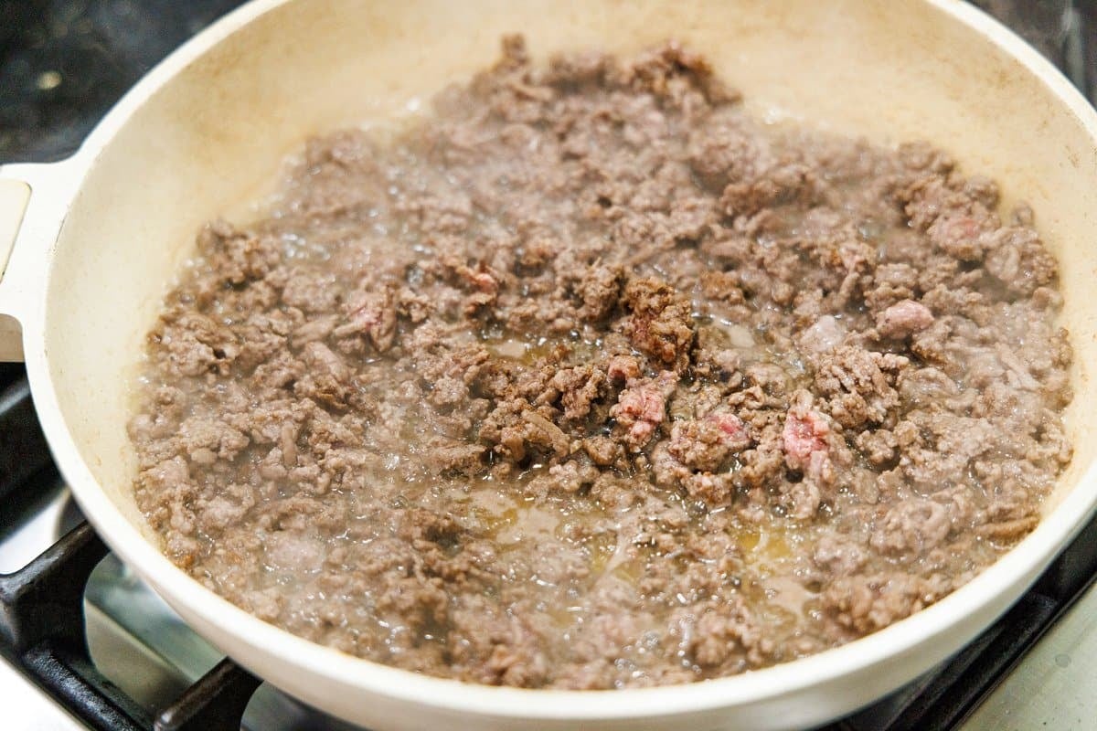 Cooking ground lamb in a large white pan.