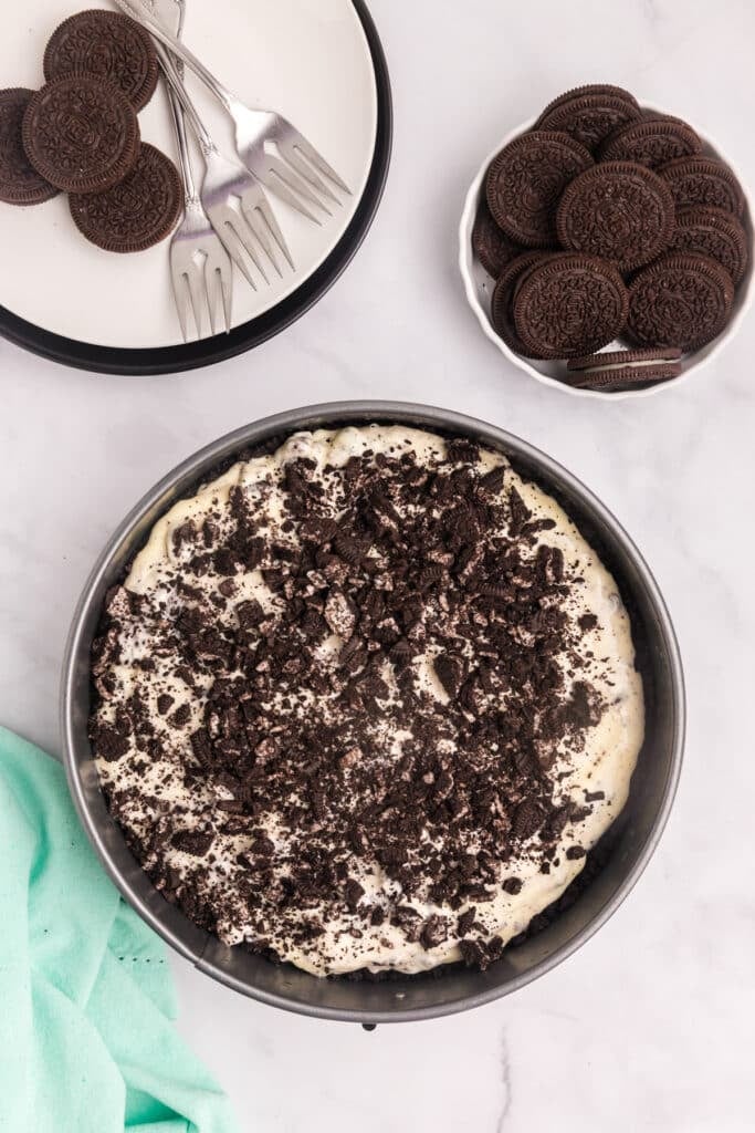 A cheesecake pan filled with creamy batter and generously sprinkled with crushed chocolate cookies, ready for baking.