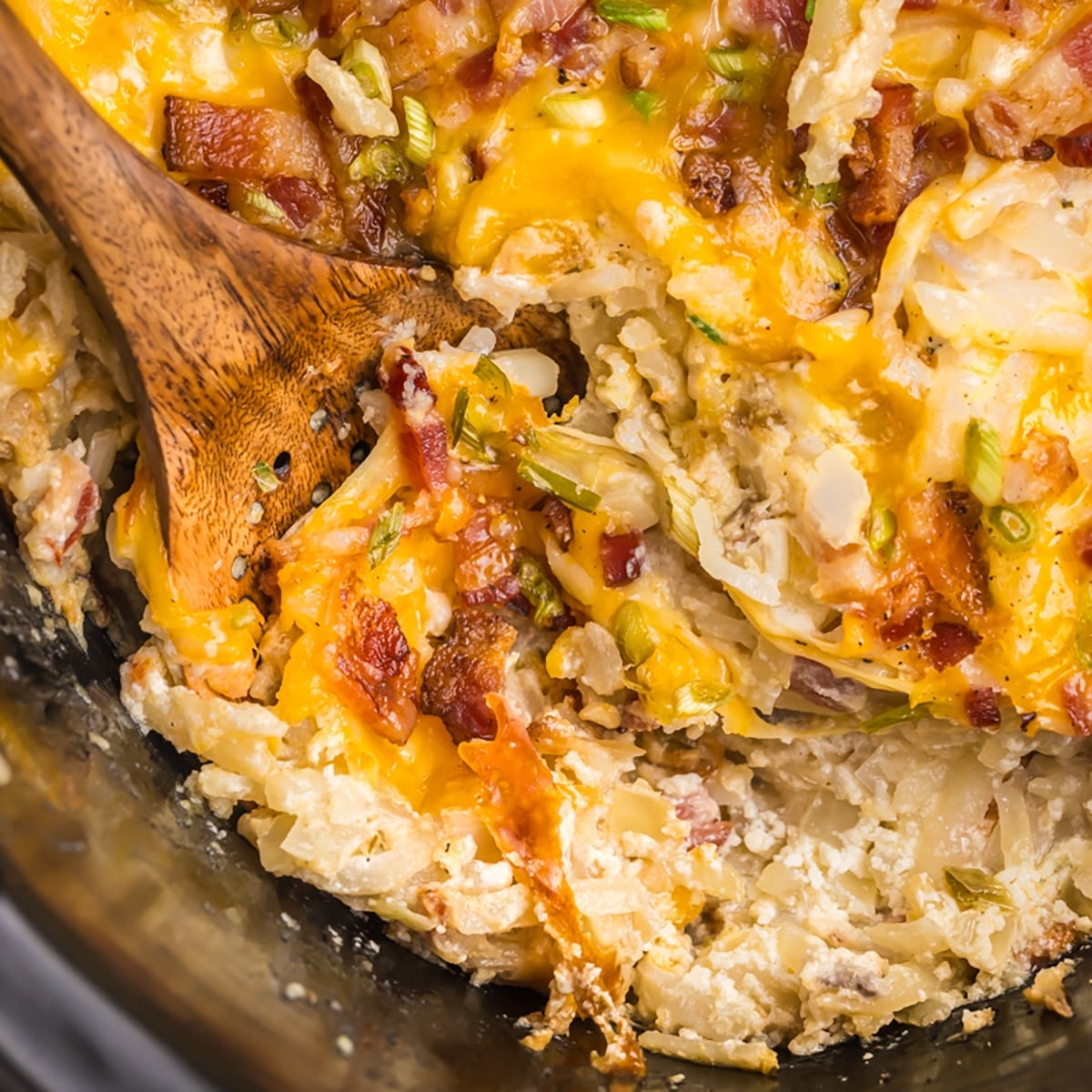 A close-up of cheesy hash brown casserole with bacon and scallions.