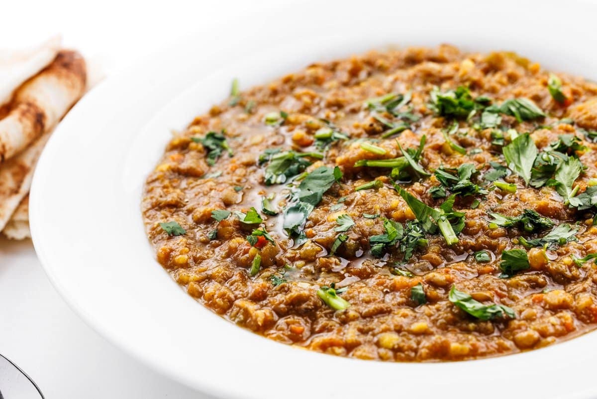 Arabic lentil soup in a wide, white bowl and garnished with fresh parsley.