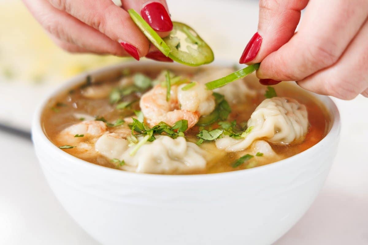 Garnishing soup with slices of jalapeño and fresh herbs.
