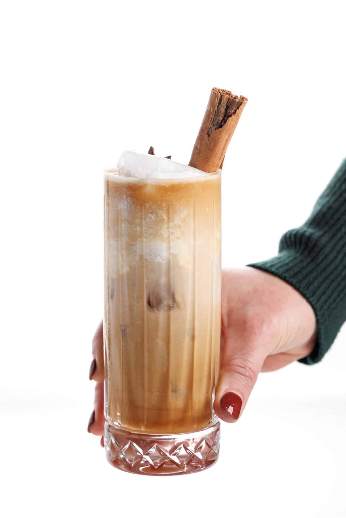 Hand holding a chai infused white Russian in a tall glass.