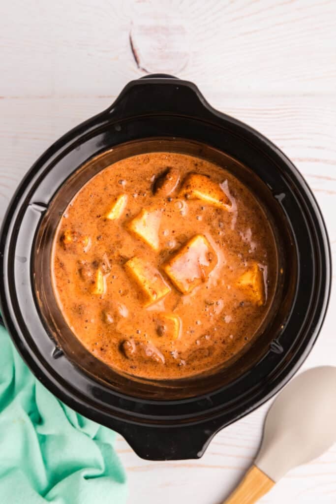 A crockpot with queso dip ingredients melting together, including chunks of cheese.