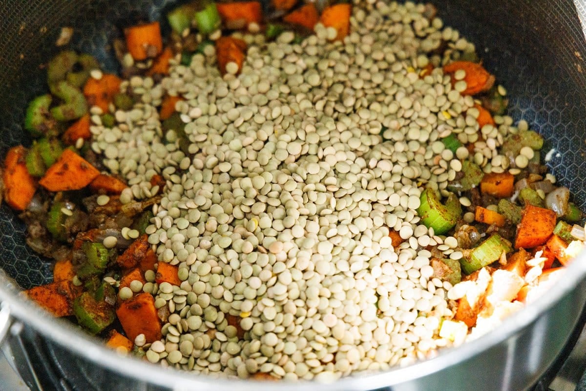 Dry brown lentils added to cooked vegetables in soup pot.