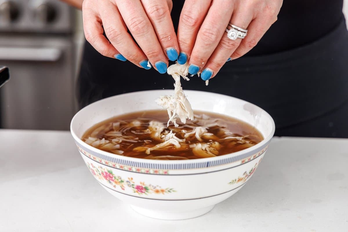 Adding shredded chicken to bowl of soup.