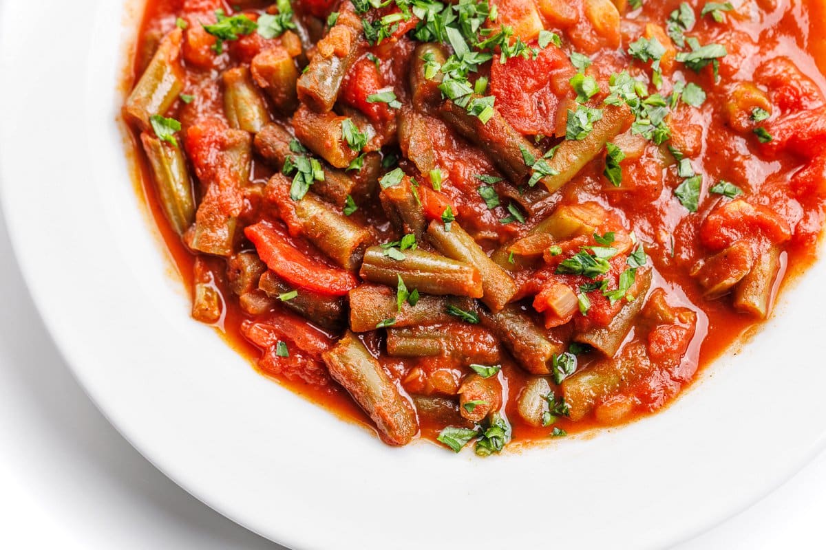An up close view of Lebanese green beans with tomatoes from the top in a white bowl.