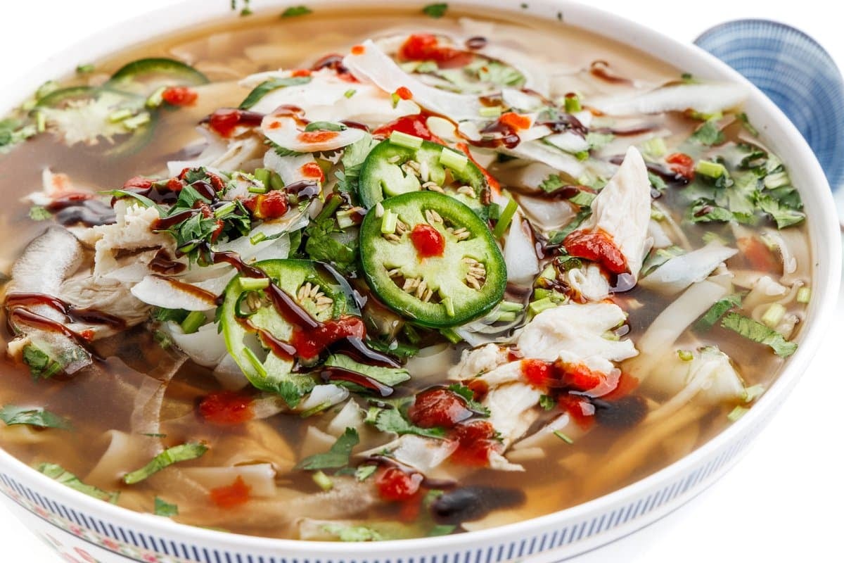 Slow cooker pho-inspired chicken soup in a white bowl garnished with toppings.