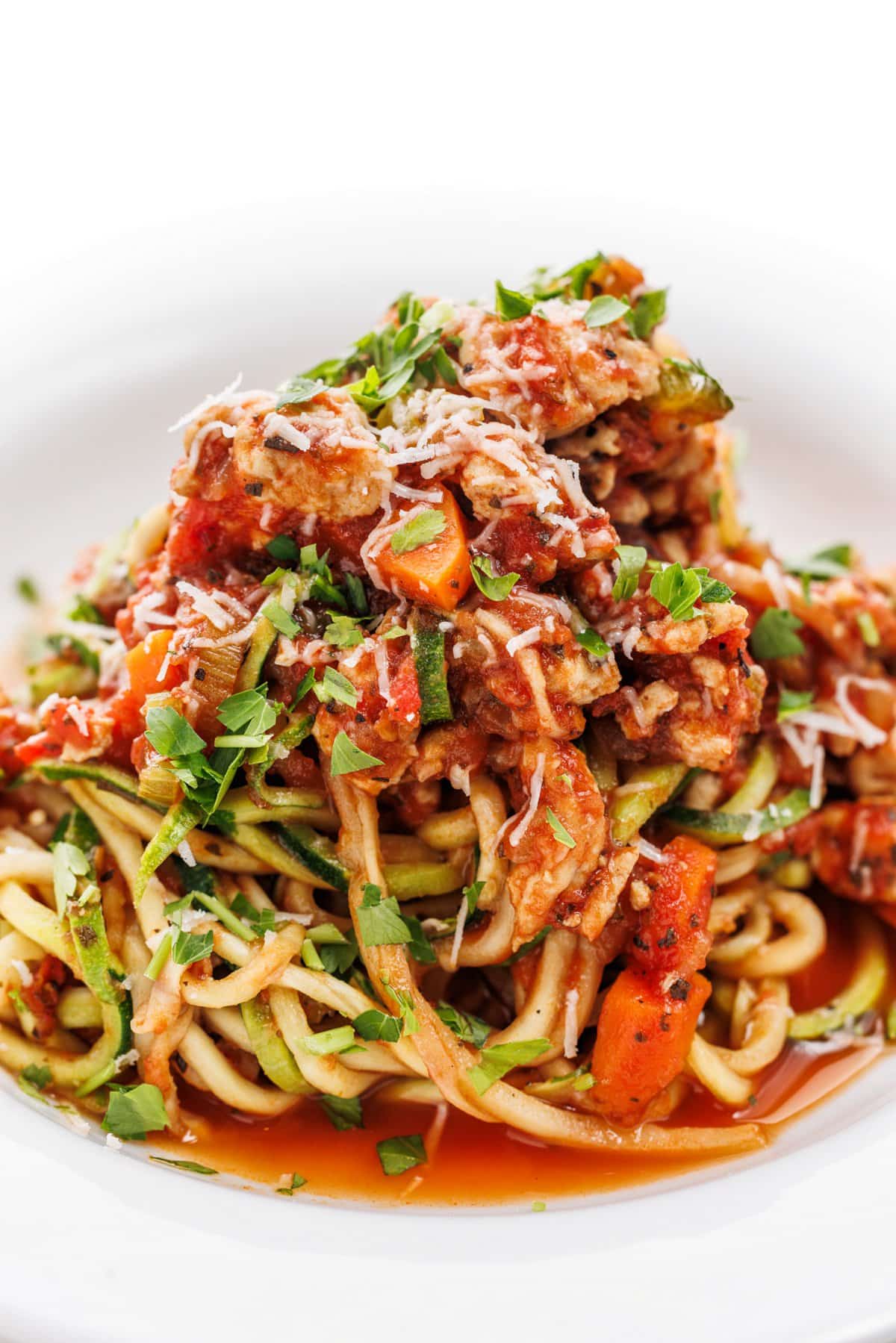 Turkey bolognese zucchini noodles garnished with parmesan cheese and fresh parsley.