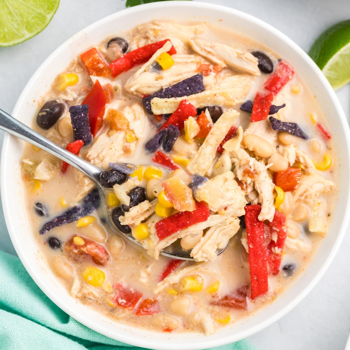 Close-up of a bowl of chicken tortilla soup with shredded chicken, beans, corn, and colorful tortilla strips, with fresh cilantro in the background.