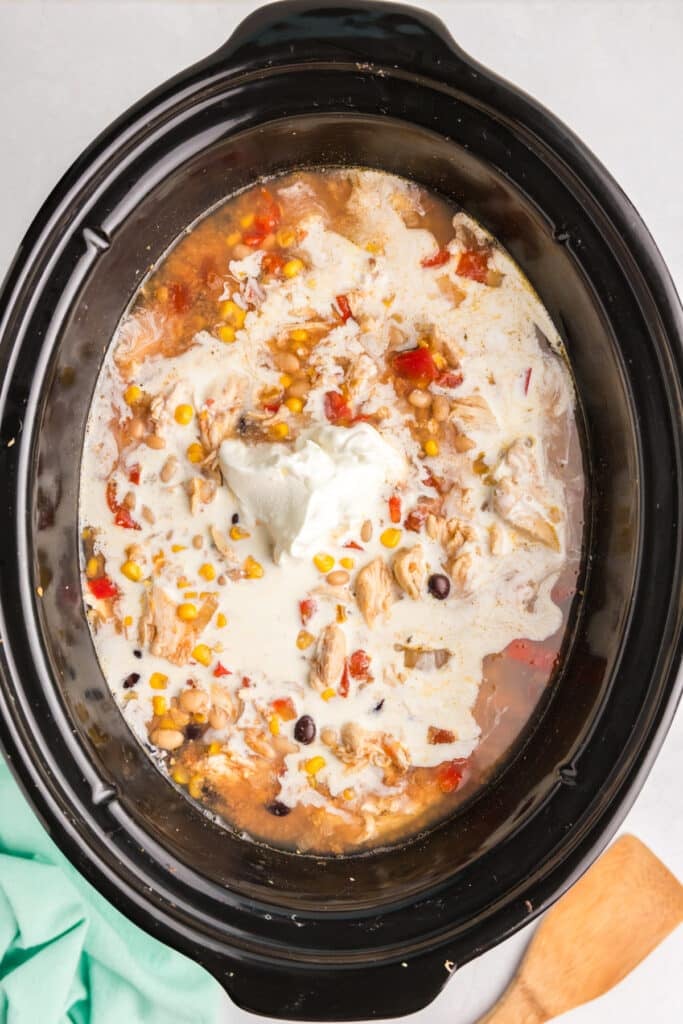 heavy cream and sour cream going into a slow cooker of tortilla soup.