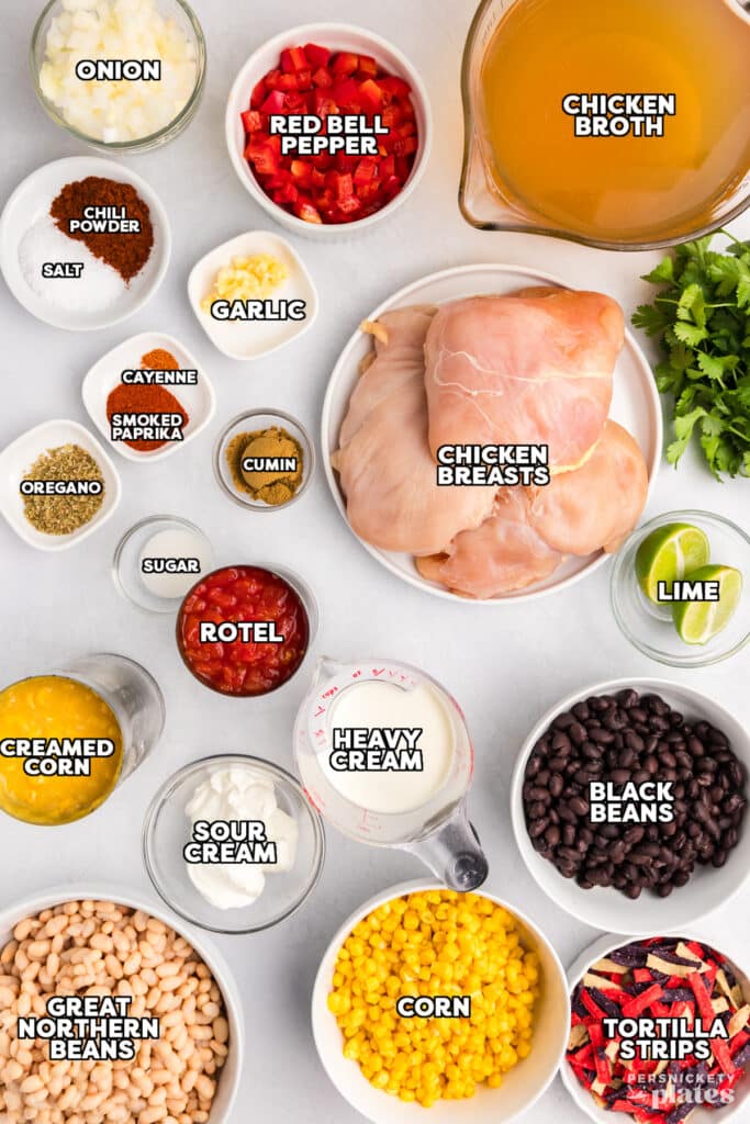 Flat lay of chicken tortilla soup ingredients, including raw chicken breasts, black beans, corn, Rotel, heavy cream, spices, and tortilla strips, all labeled.