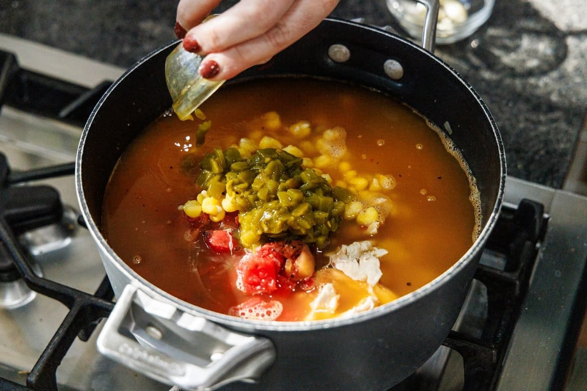 Green chiles being added to pozole in pot.