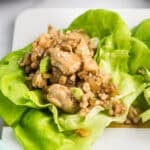 Chicken lettuce wrap with sesame seeds on a wooden board.