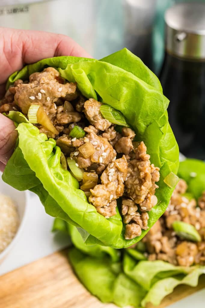 Hand holding a chicken lettuce wrap with sesame seeds.